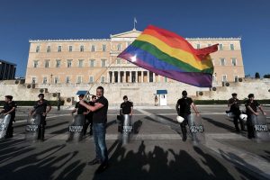 A participant of the  Gay Pride event  waves a rainbow flag by police protecting the Greek parliament in central  Athens on June 9, 2012. Some 1000 people took part at a march organised by Greece's gay and lesbian community, with the main slogan ' love me, its for free' . AFP PHOTO/ LOUISA GOULIAMAKIARIS MESSINIS/AFP/GettyImages ORG XMIT: